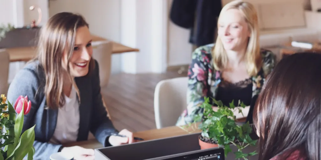 Three professional women collaborating on a business project, discussing documents on a laptop. Digital marketing in times of recession